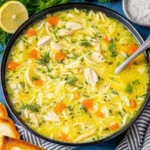 A bowl of creamy Greek lemon chicken soup (Avgolemono) with orzo pasta, shredded chicken, and a garnish of fresh dill.
