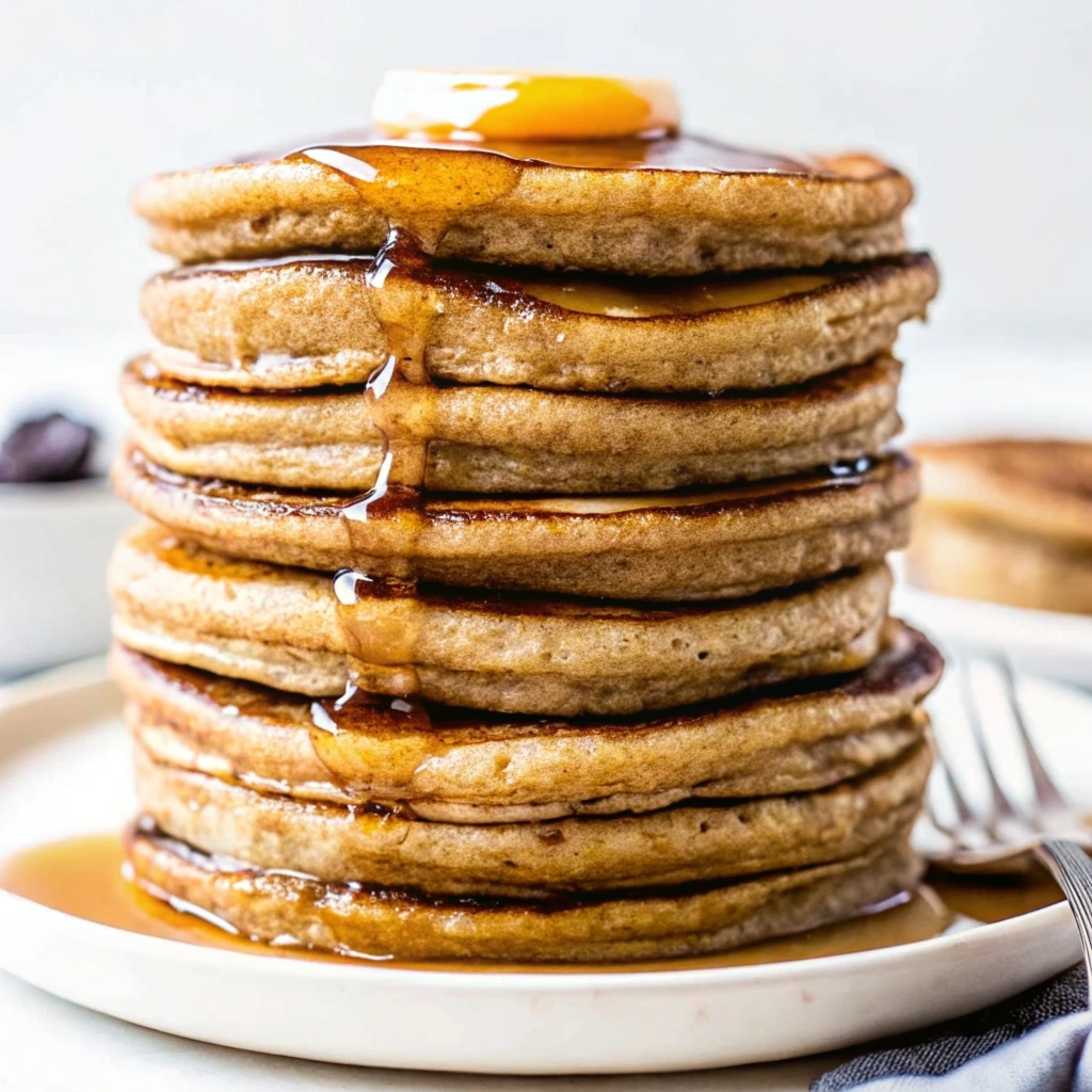 A stack of fluffy gluten-free banana oat pancakes with maple syrup and fresh banana slices on a plate.