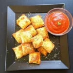 Crispy toasted ravioli in an air fryer basket with marinara sauce.
